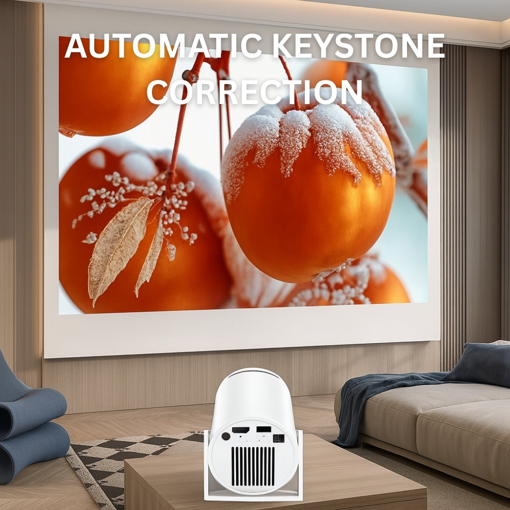 The NEW Spotlight Projector by The Projection Room displays a frosty orange fruit image with "AUTOMATIC KEYSTONE CORRECTION" text in a modern living room, where a couch and rolled-up mats are also visible.