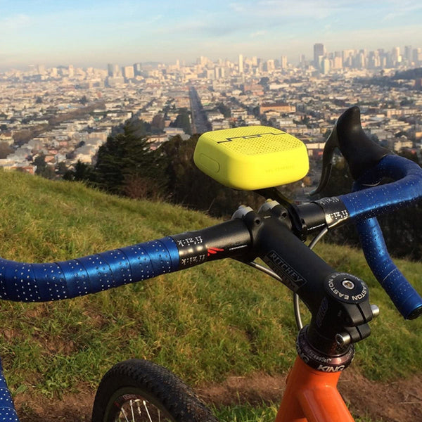 A bicycle with blue handlebar tape and a SOL Republic Punk Wireless Pocket Speaker from The Projection Room, featuring impressive Bluetooth range, is parked on a grassy hill overlooking a sprawling cityscape under a clear sky.