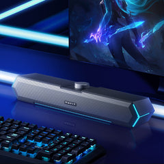 A stylish The Projection Room RGB Bluetooth Speakers with RGB lighting sits on a glossy desk in front of gaming speakers, keyboard, and monitor, featuring a handy 3.5MM audio jack for easy connectivity.