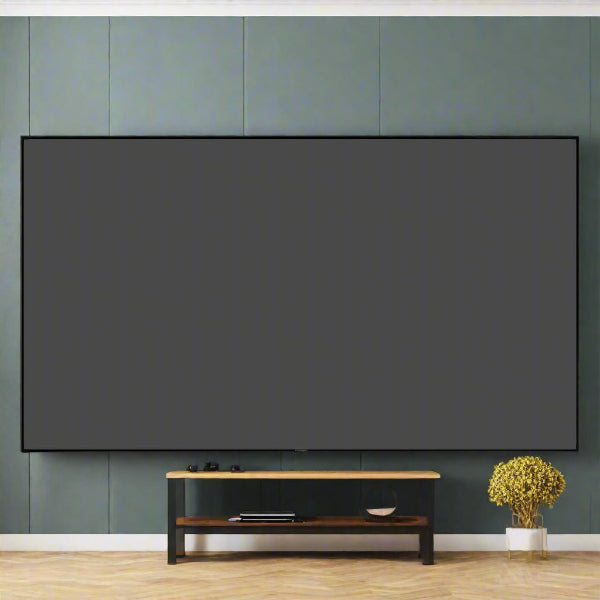 A large WUPRO Black Crystal ALR Fixed Projector Screen for 4K/8K UHD is mounted on a green wall above a minimalist black and wooden TV stand, holding a book and small object. To the right, the floor is brightened by a potted plant with yellow flowers.